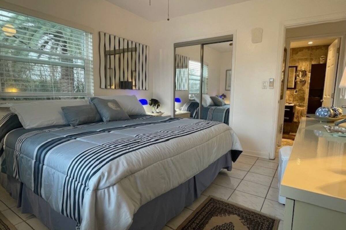 A modern bedroom with a large bed, a bedside table, a mirror, and a view of the bathroom.