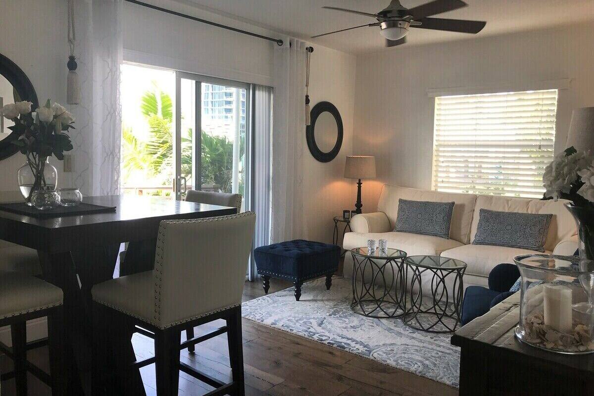 A living room with a sofa, ottoman, and coffee table, a dining area with a table and chairs, and a ceiling fan.