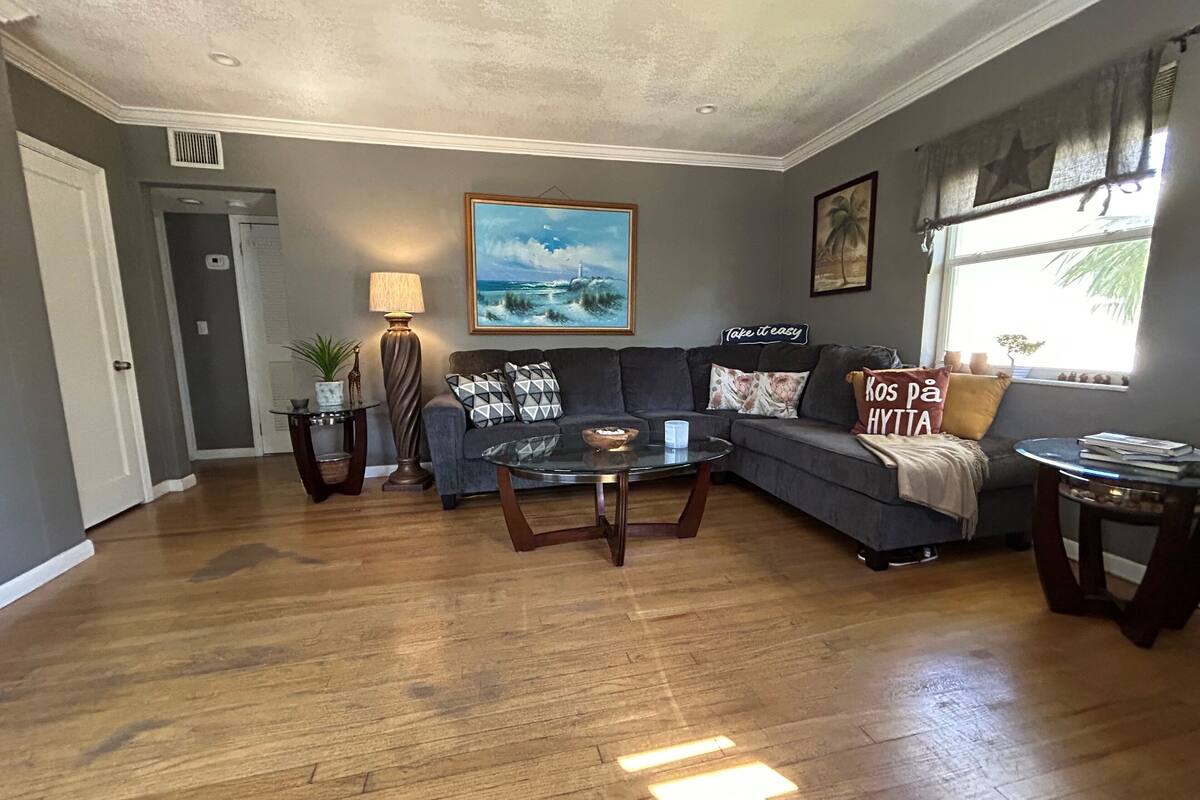 A living room with a gray sofa, a glass coffee table, and a painting of a seascape.