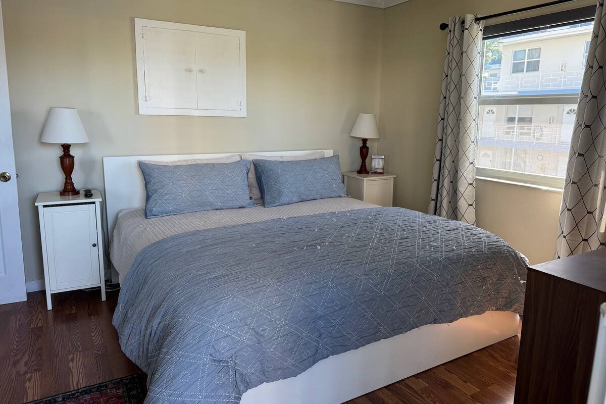 A bedroom with a bed, two bedside tables, a nightstand, a window with curtains, and a door.
