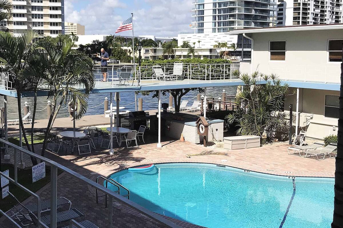A swimming pool with a lifeguard stand, lounge chairs, and a view of a marina with boats.