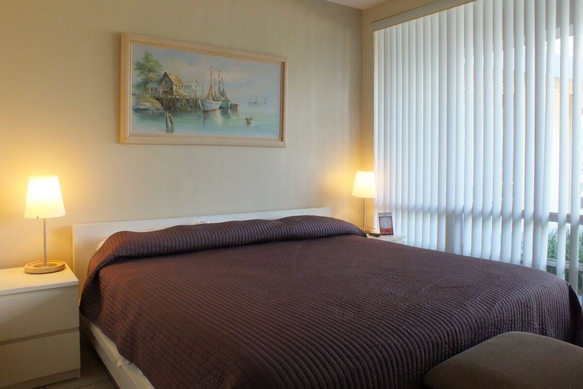 A hotel room with a large bed, two bedside lamps, a painting on the wall, and a window with blinds.