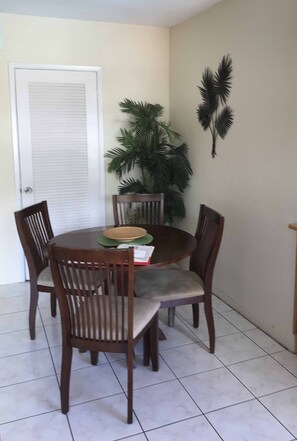 A dining area with a round table, four wooden chairs, a woven placemat, and a potted plant. - Holiday Isle Yacht Club (Fort Lauderdale)