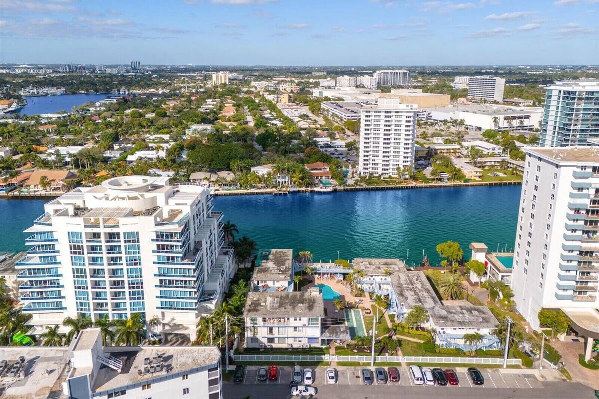 A high-rise hotel with multiple floors, a swimming pool, and a marina in the background.