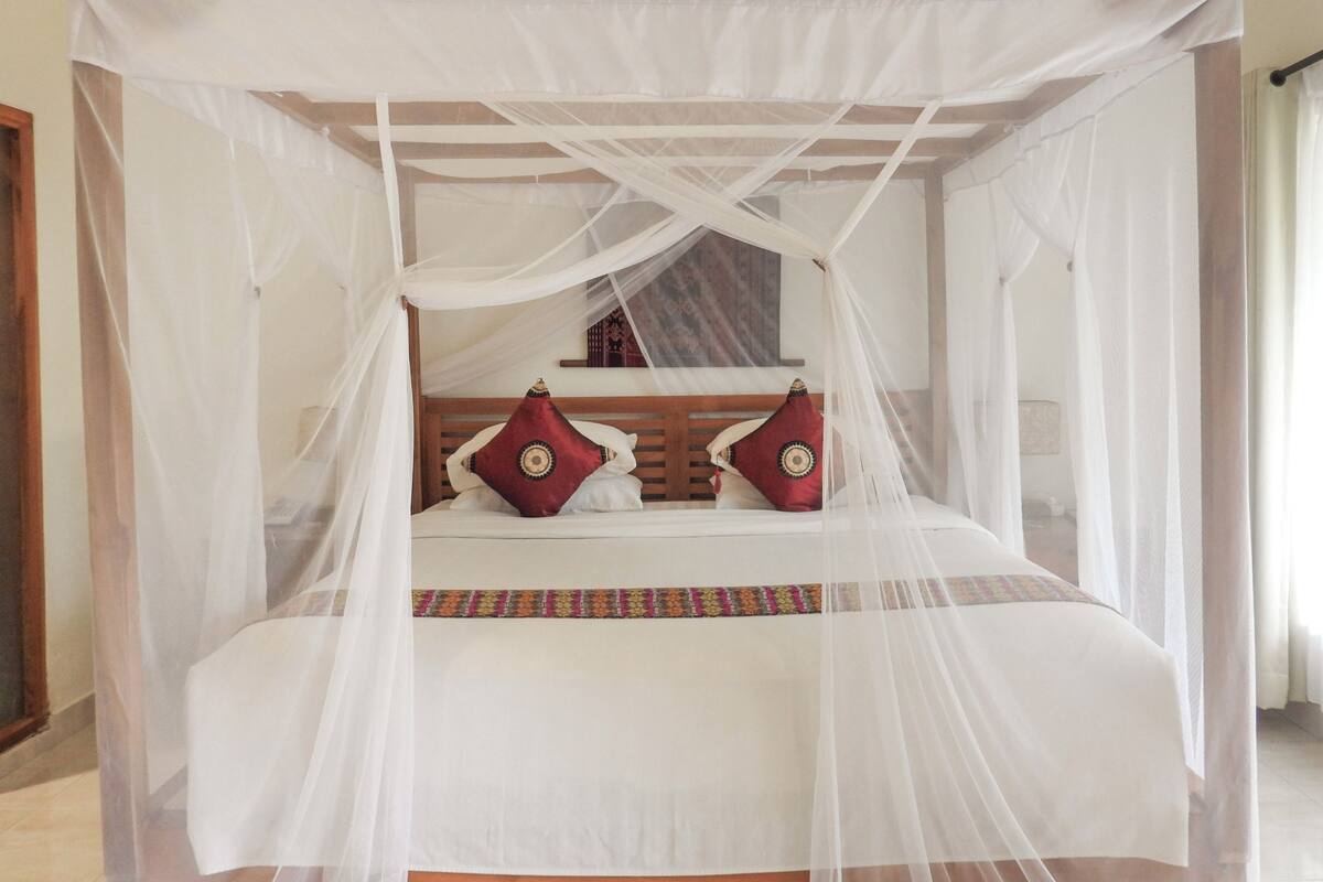 A bed with a canopy, two pillows, and a patterned bedspread.