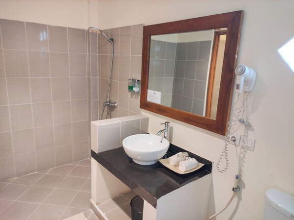 Un baño con ducha, un lavabo con espejo y un secador de pelo en la pared.
