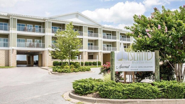 A multi-story hotel with balconies, a covered parking area, and a sign indicating it is a member of the Ascend Hotel Collection.