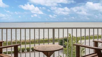 A balcony with a view of the sea, a small round table, and two wooden chairs.