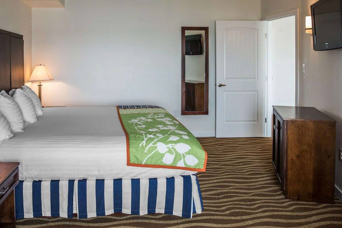 A hotel room with a bed, a bedside lamp, a door, a television on the wall, and a striped rug.