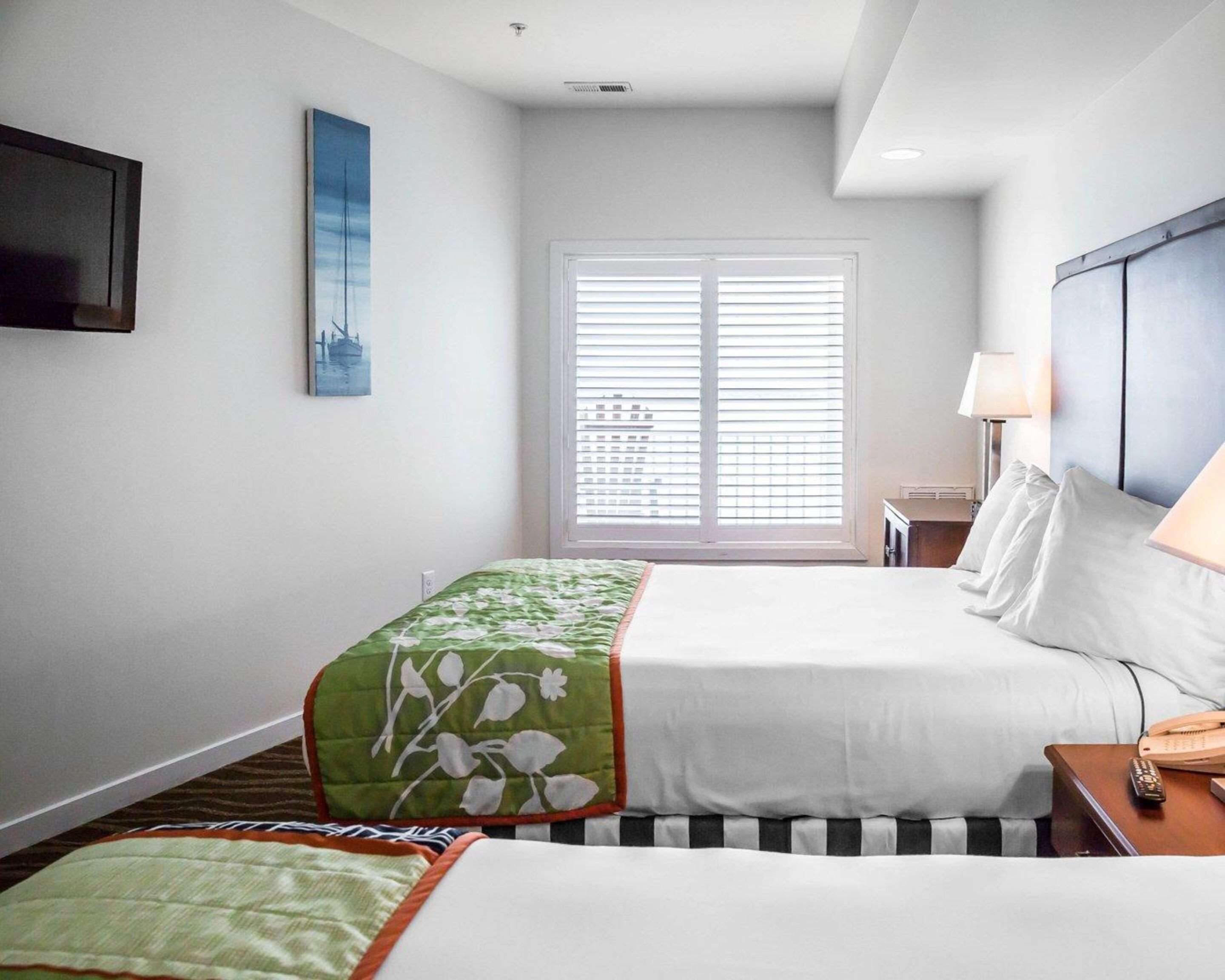 Een hotelkamer met een bed, een nachtkastje met een lamp, een raam met zonwering en een aan de muur bevestigde televisie.