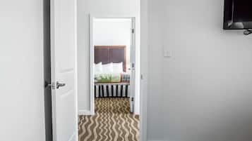 A hotel room with a bed, a television mounted on the wall, and a door leading to another room.