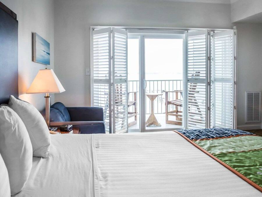 Una habitación de hotel con cama, una silla, una lámpara y un balcón con mesa y sillas.