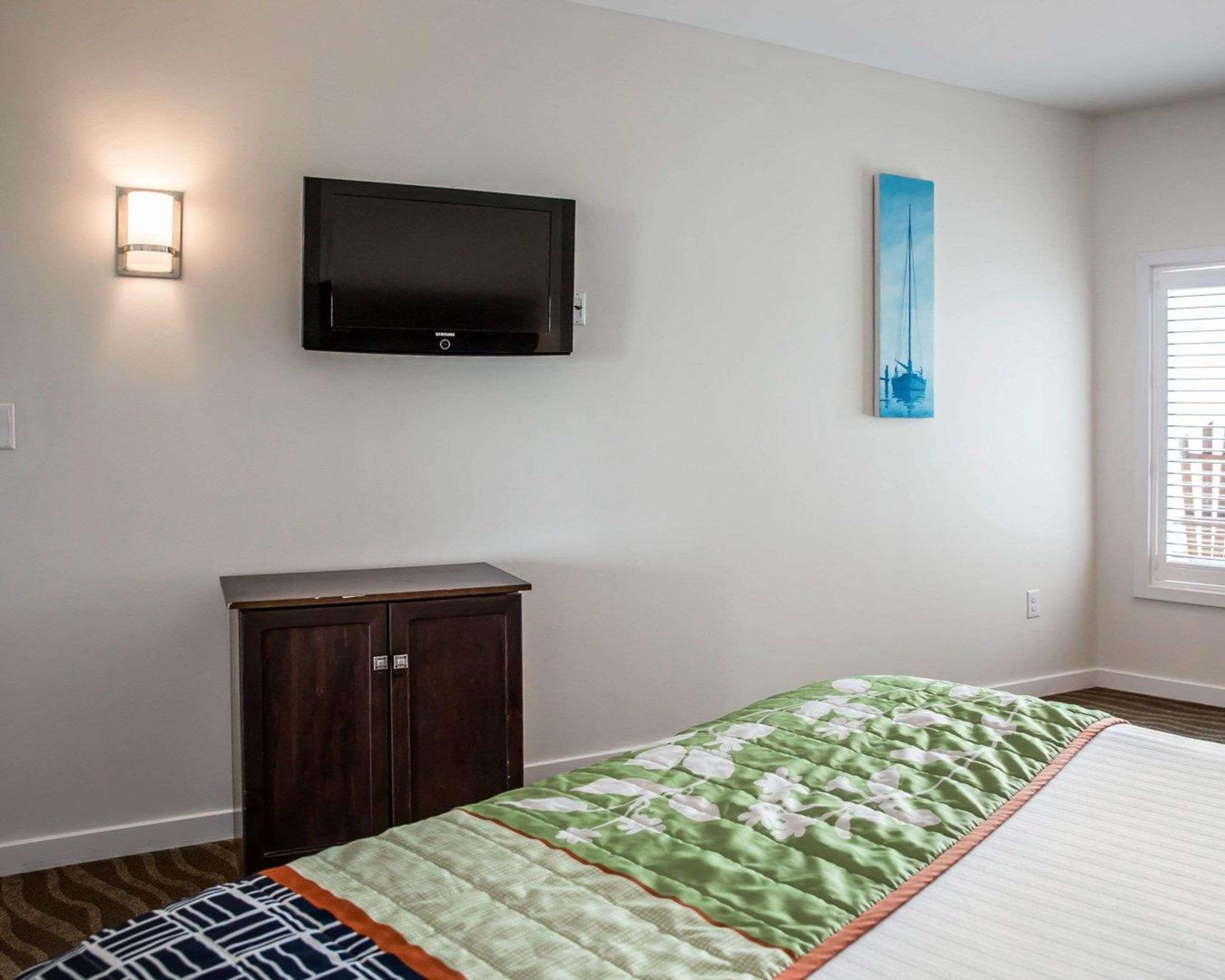 A bedroom with a bed, a TV mounted on the wall, a cabinet, and a painting.