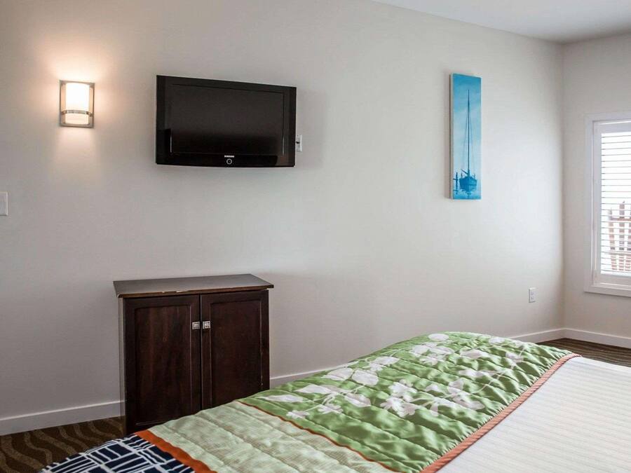 A bedroom with a bed, a TV mounted on the wall, a cabinet, and a painting.