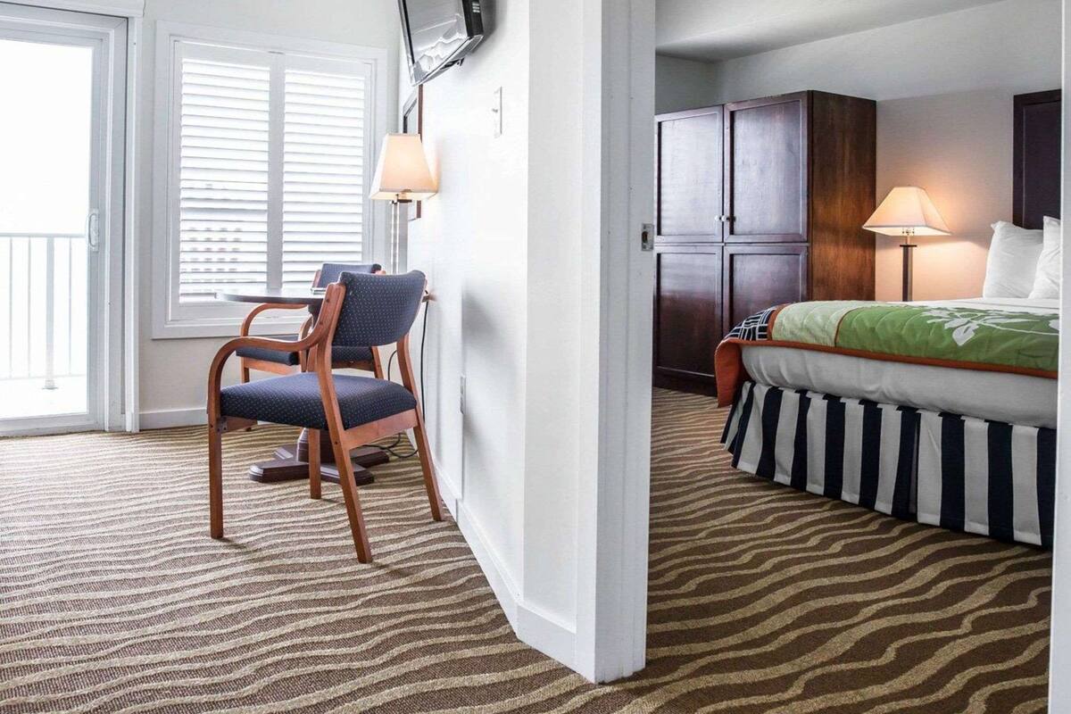 A hotel room with a bed, a chair, a TV, a wardrobe, and a window with blinds.