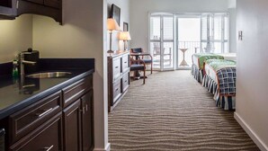 Un pasillo estrecho que da a un balcón con vistas, una kitchenette con armarios oscuros y una alfombra estampada.