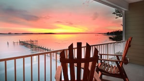 A wooden chair on a balcony overlooking a sunset over a body of water.
