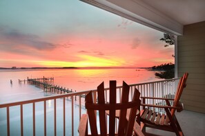 A wooden chair on a balcony overlooking a sunset over a body of water.