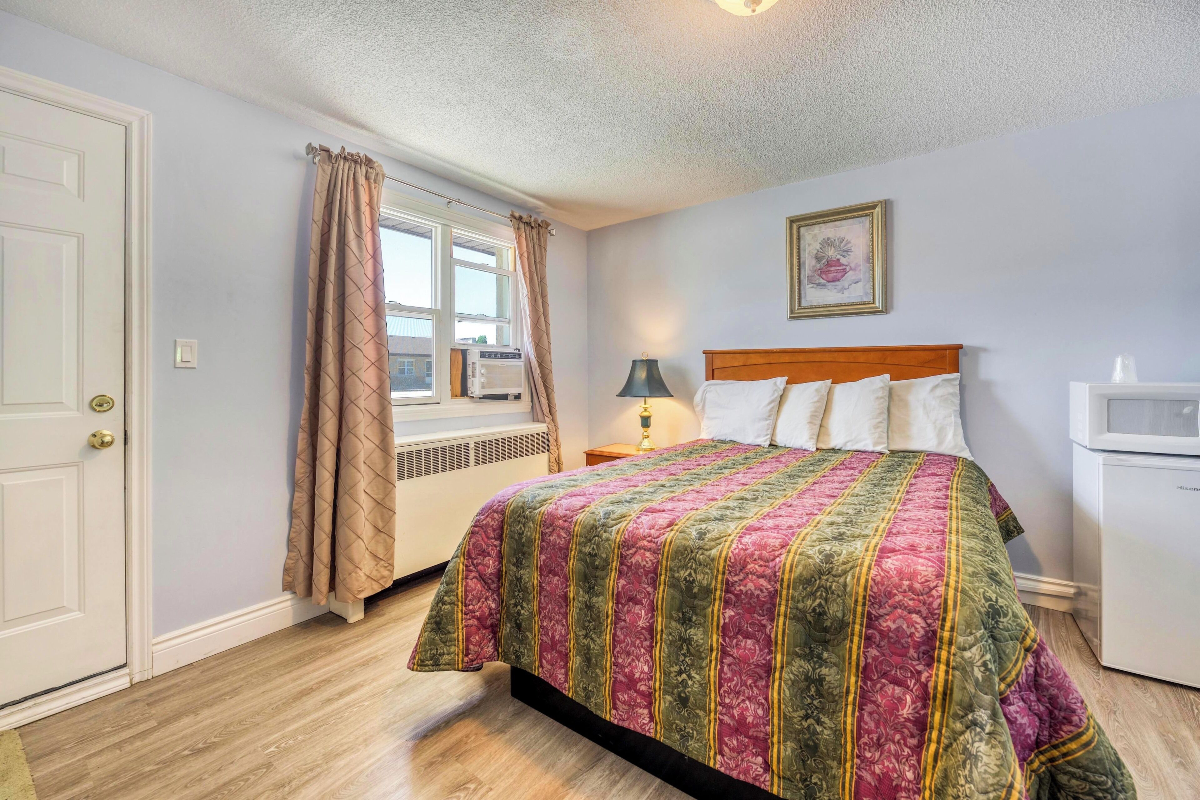 A bedroom with a bed, a bedside table with a lamp, a window with curtains, and a radiator.