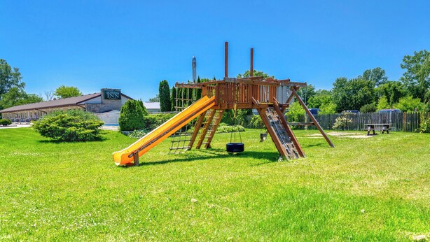 A playground with a slide and swings in a grassy area with a building in the background. - The Gables inn (Sarnia)