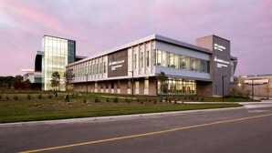 A modern building with a glass facade, a flat roof, and a parking lot in front. - The Gables inn (Sarnia)