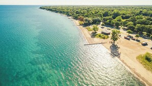 An aerial view of a coastal area with a beach, dense greenery, and clear turquoise waters. - The Gables inn (Sarnia)