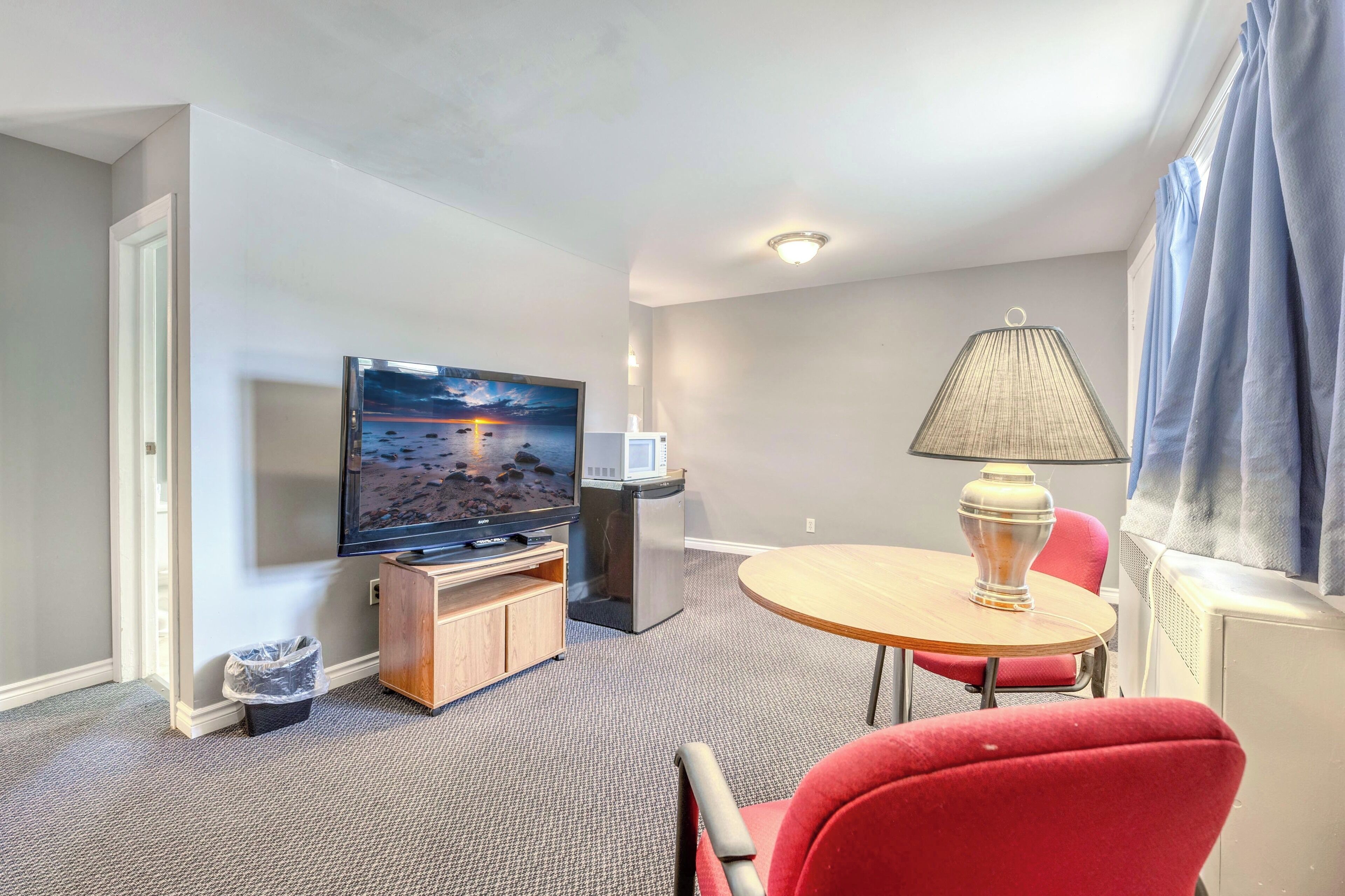 Una habitación de hotel con televisión, una mesita, una lámpara y una silla roja.