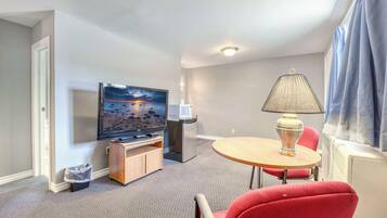 Una habitación de hotel con televisión, una mesita, una lámpara y una silla roja.