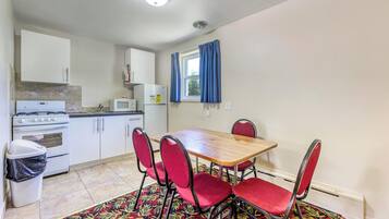 A compact kitchen with white cabinets, a stove, a microwave, and a window with blue curtains.