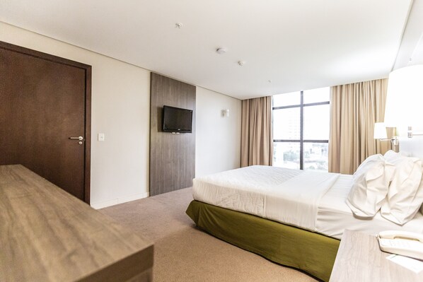 A hotel room with a bed, a television, a window with curtains, and a desk.