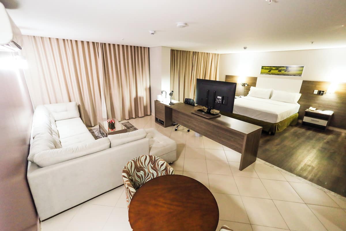 A hotel room with a sofa, a small round table, a TV, a bed, and a desk.