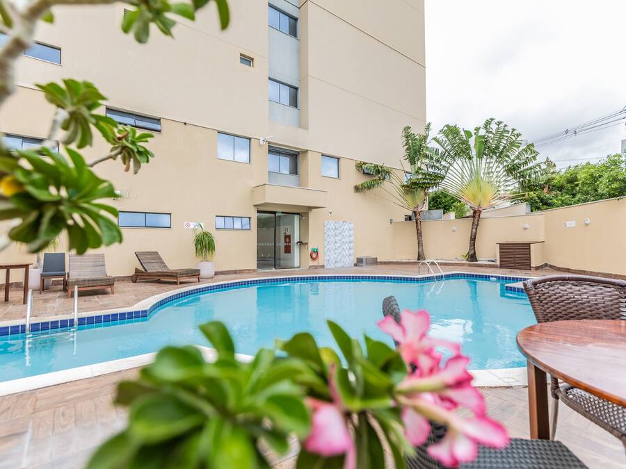 Una piscina con sillas de descanso y una mesa, rodeada por un edificio con varias ventanas y una puerta.
