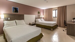 Hotellihuone, jossa on kaksi sänkyä, työpöytä, lamppu ja ikkuna, jossa on verhot.