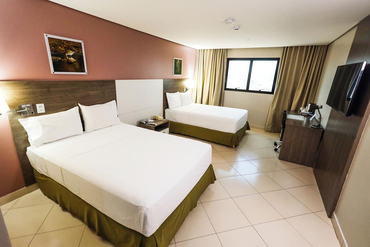 A hotel room with two beds, a TV, a desk, and a window with curtains.