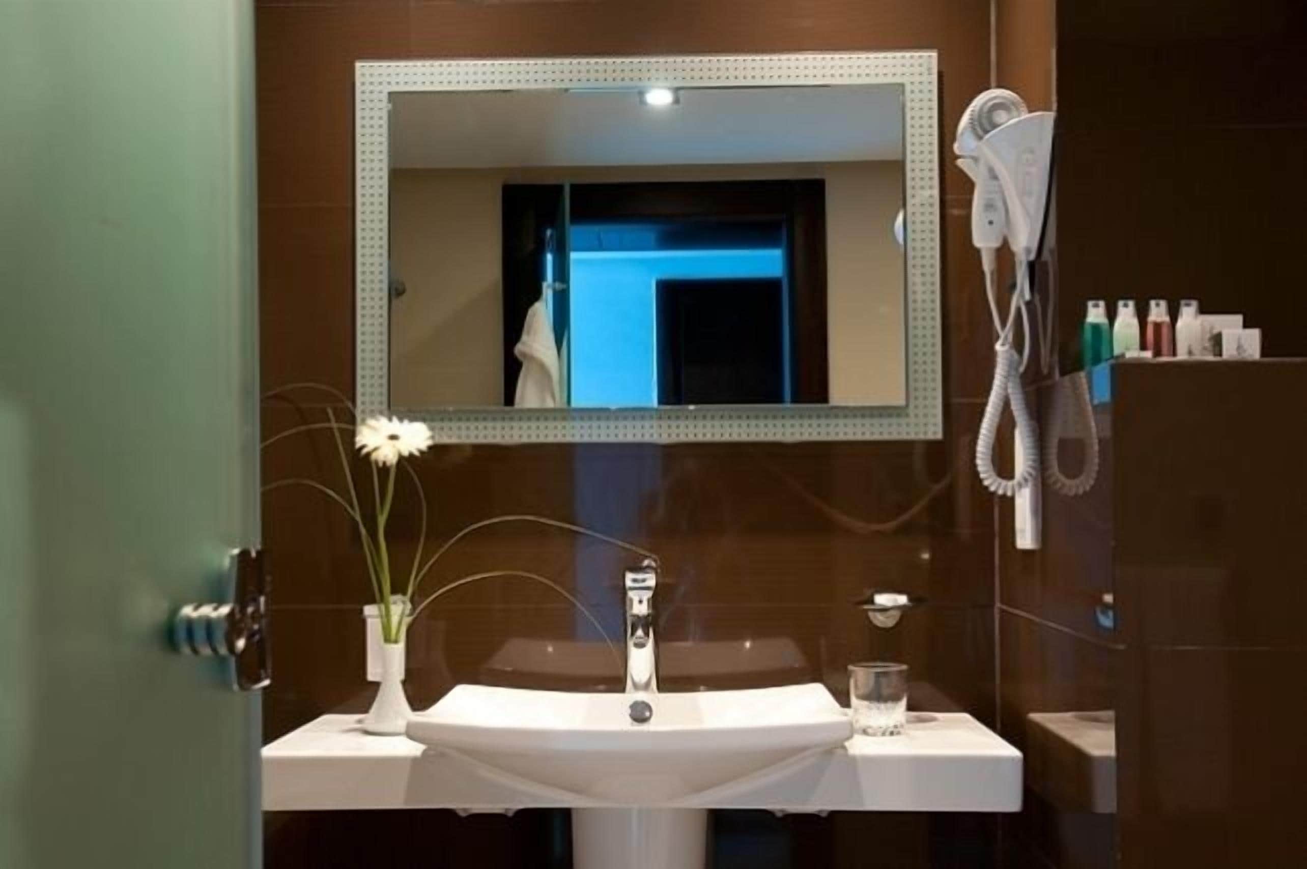 Un baño con lavamanos blanco, un espejo y un secador de pelo en la pared.