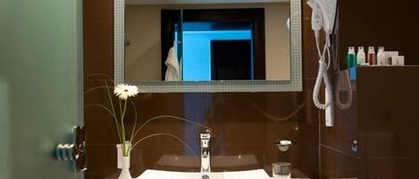 Un baño con lavamanos blanco, un espejo y un secador de pelo en la pared.