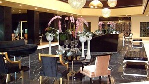 Een moderne lobby met een zwart receptiebalie, meerdere zithoeken en decoratieve vazen met bloemen.
