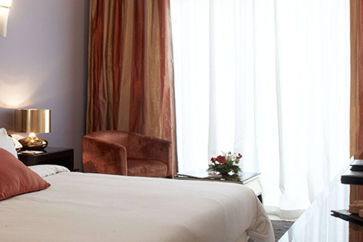 Une chambre d’hôtel avec un grand lit, deux tables de chevet, une chaise et une petite table avec une lampe.