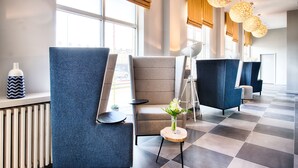A modern waiting area with blue and grey chairs, a small table with a vase, and large windows with natural light. - Leonardo Hotel Edinburgh Haymarket (Edinburgh)