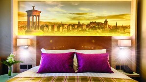 A hotel room with a large bed, two pillows, a nightstand, a lamp, and a framed cityscape picture on the wall. - Leonardo Hotel Edinburgh Haymarket (Edinburgh)