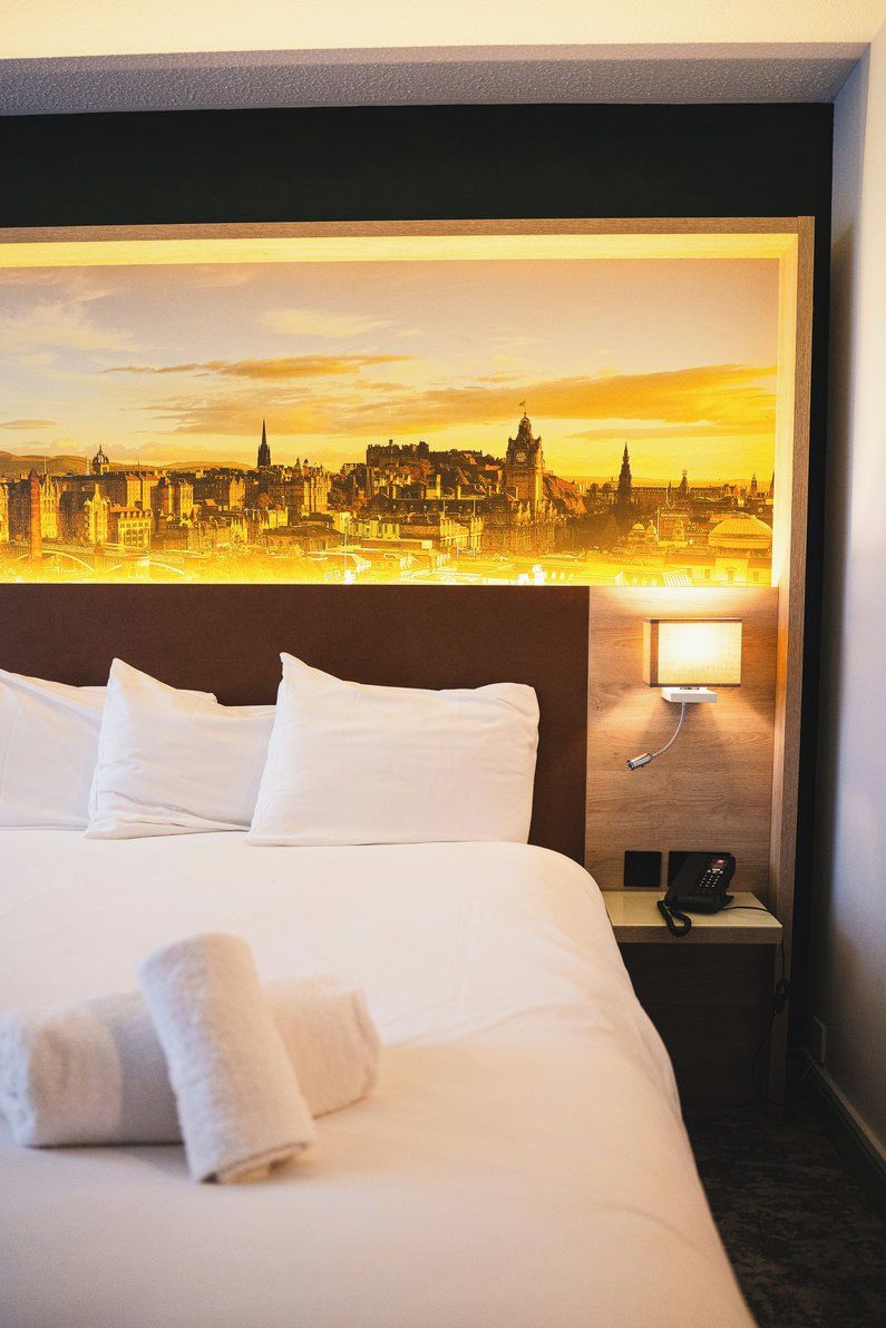 Een hotelkamer met een bed, kussens, een nachtkastje met telefoon en een wandlamp.