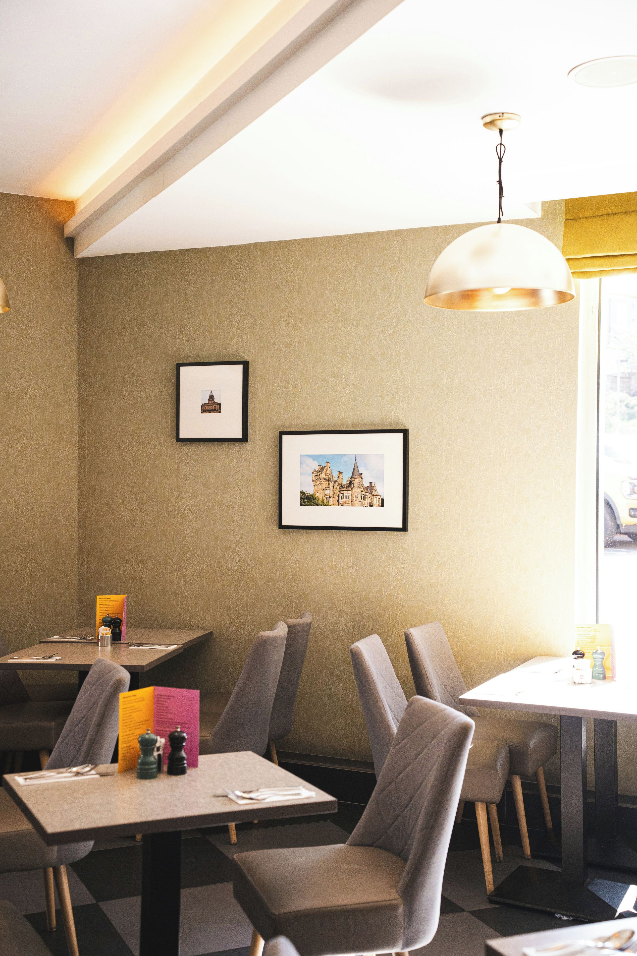 Un interior de restaurante con mesas, sillas, cuadros en la pared y una lámpara colgante.