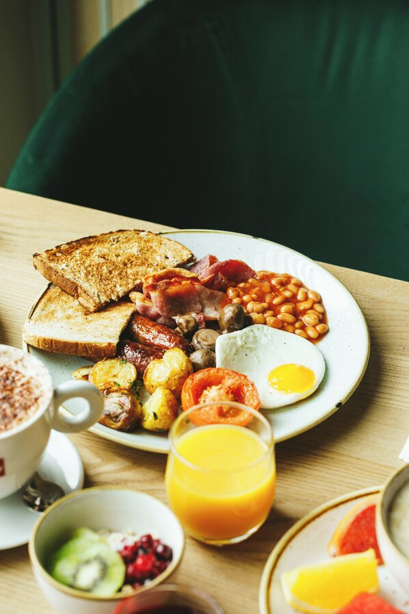 A breakfast plate with toast, eggs, sausages, beans, and a glass of orange juice.