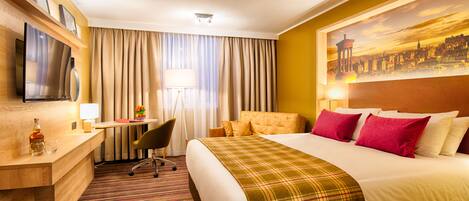 A hotel room with a bed, a desk, a chair, a television, and a painting on the wall.