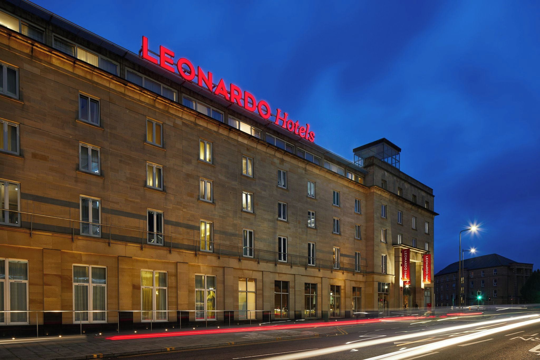 Um edifício de hotel com vários andares e uma placa vermelha chamativa com a inscrição 'LEONARDO Hotels'.