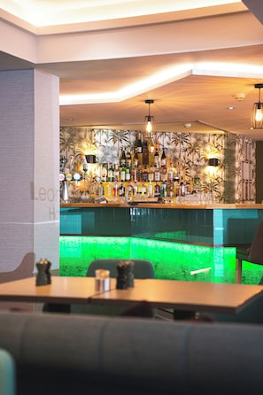 A bar area with a variety of liquor bottles, a green illuminated bar counter, and hanging pendant lights. - Leonardo Hotel Edinburgh Haymarket (Edinburgh)