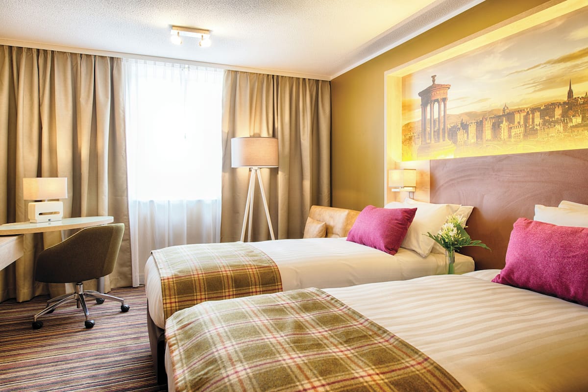 A hotel room with two beds, a desk, and a chair.