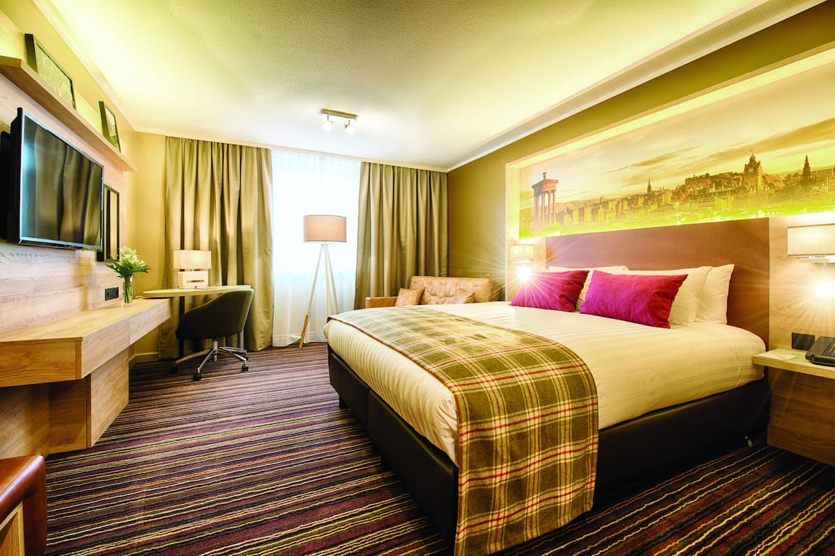 A hotel room with a bed, desk, chair, and a flat-screen TV.