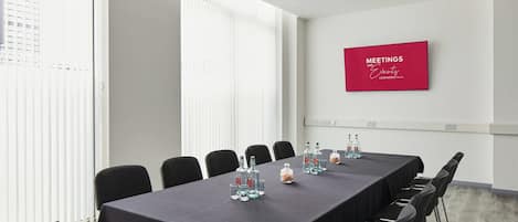 Ein Konferenzraum mit einem langen Tisch, Stühlen und einer an der Wand befestigten Beschilderung für Besprechungen und Veranstaltungen.