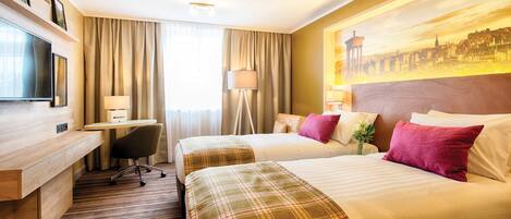 A hotel room with two beds, a desk, a chair, a TV, and a painting of a cityscape.